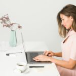 A woman in a pink dress working on a laptop at a modern, minimalist desk.